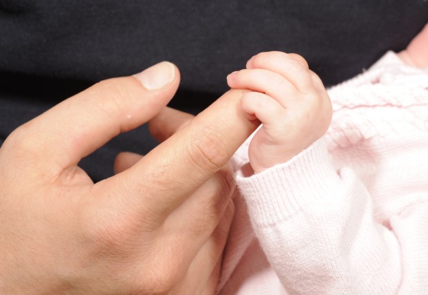 A newborn baby holding an adult's finger.