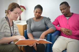 A midwife talking to couple, showing them an inheritance chart.