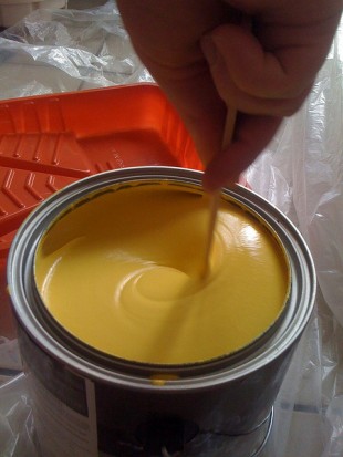 A hand stirring paint in a tin with a paintbrush.