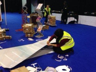 Members of staff setting up for the conference using sticky tape to put posters together.