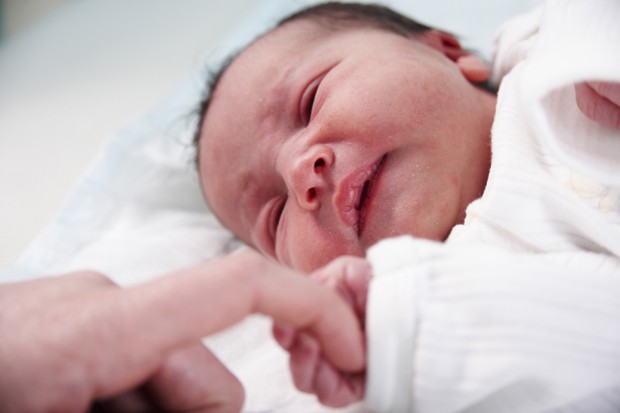 A newborn baby holding an adult's finger.