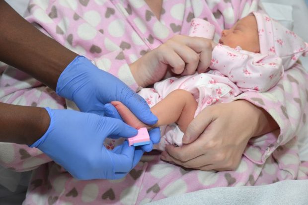 A person holding a baby while it has the heel prick test done.