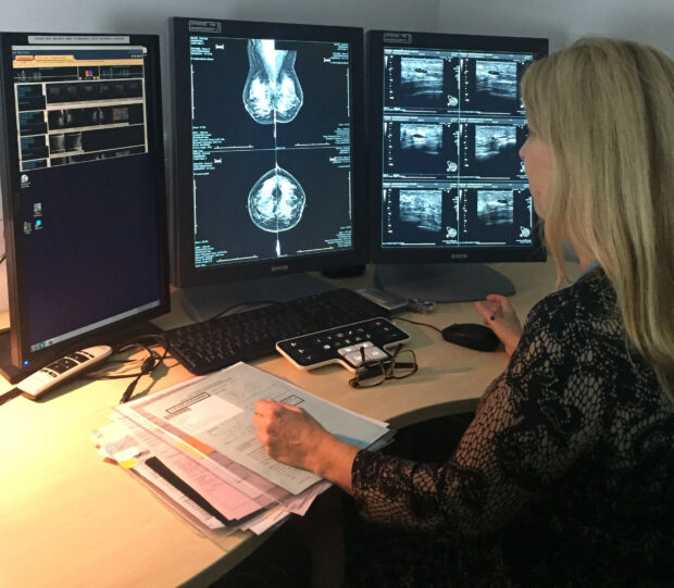 A woman at a desk looking at mammogram images on screens as part of the breast screening programme