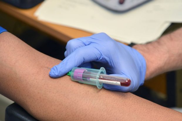 A blood sample being taken from an arm by a gloved hand.
