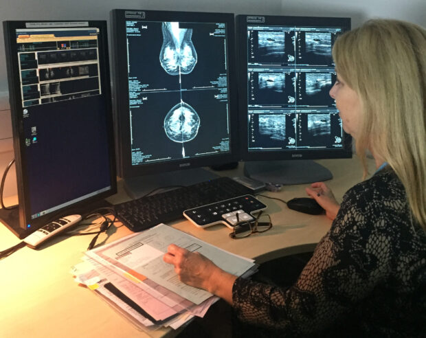 A woman reading breast screening images on several screens.