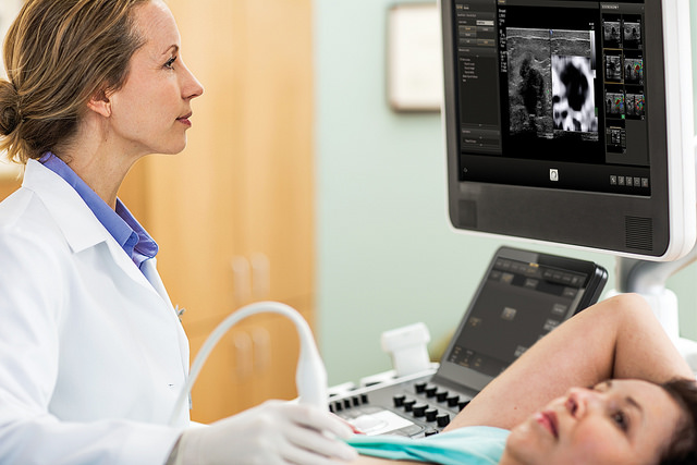 A woman having an ultrasound scan done. A medical professional is looking at the scan on a screen.