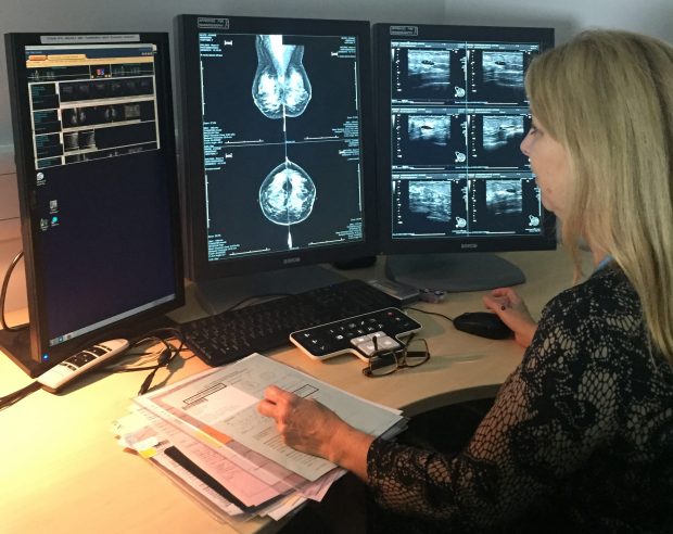 A woman at a desk looking at mammogram images on screens as part of the breast screening programme