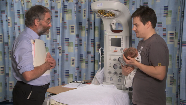 A health professional talking to a man holding a young baby.
