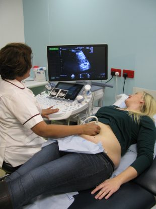 A woman having an ultrasound scan performed by another woman. They are both looking at the scan on a screen.