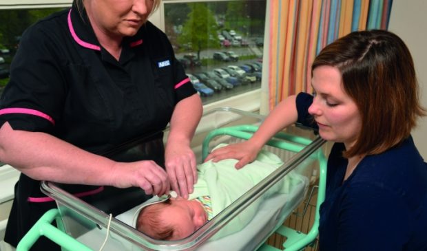 A baby undergoing newborn hearing screening with the mother looking on.