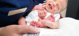 Baby and a nurse. The nurse is taking a blood sample from the baby's heel.