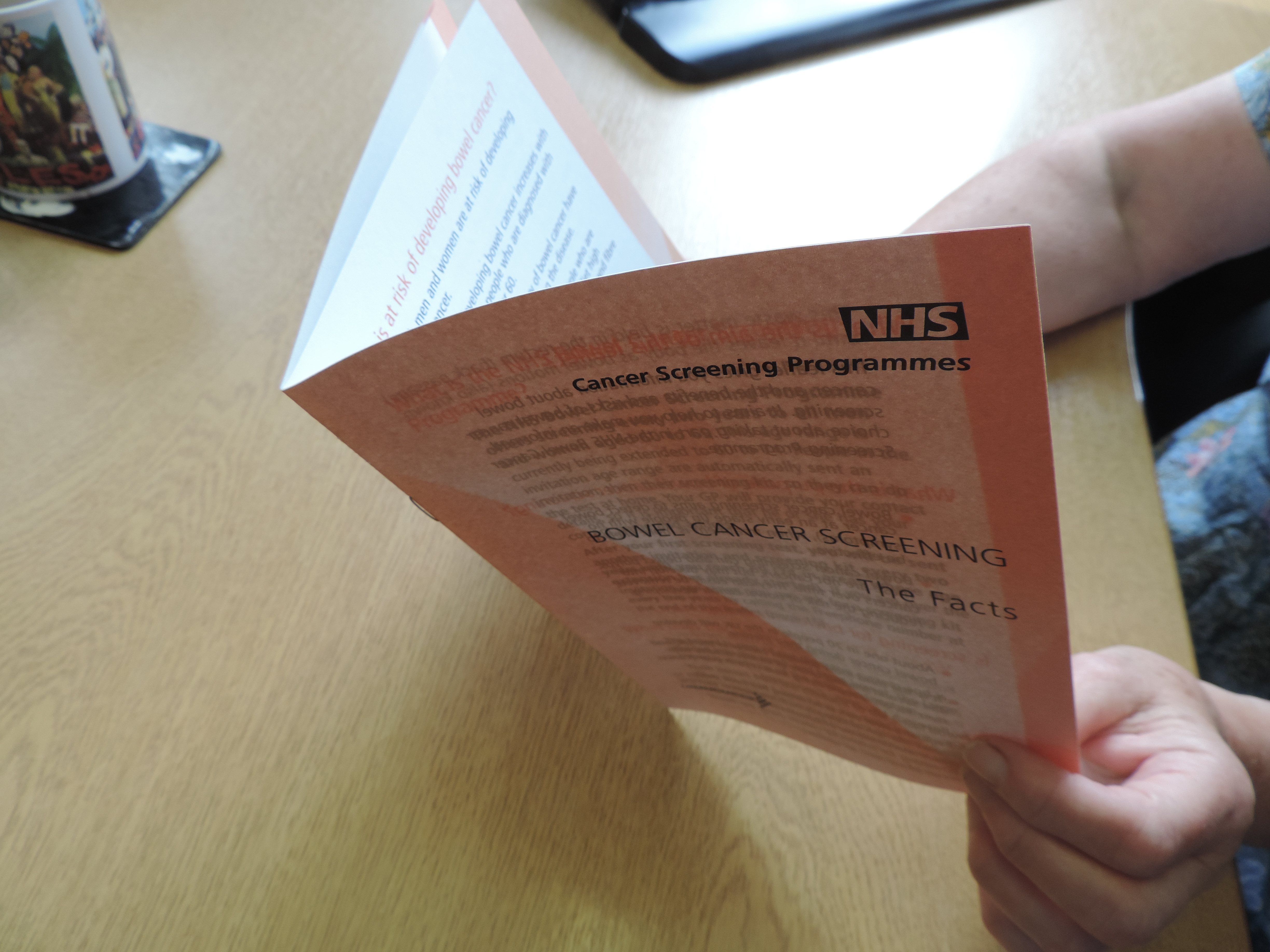 A woman reading the current bowel cancer screening leaflet. The front of the leaflet says 'Bowel cancer screening: the facts'.