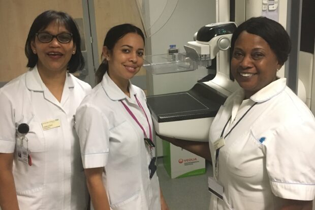 3 mammographers stood in front of a machine.