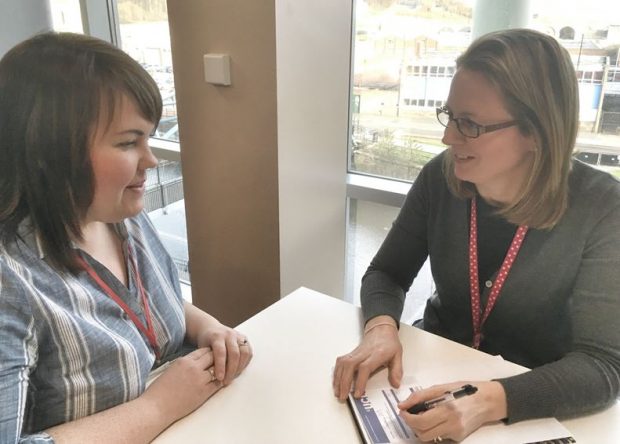 Two women talking to each other with one woman holding a pen and asking the women some questions