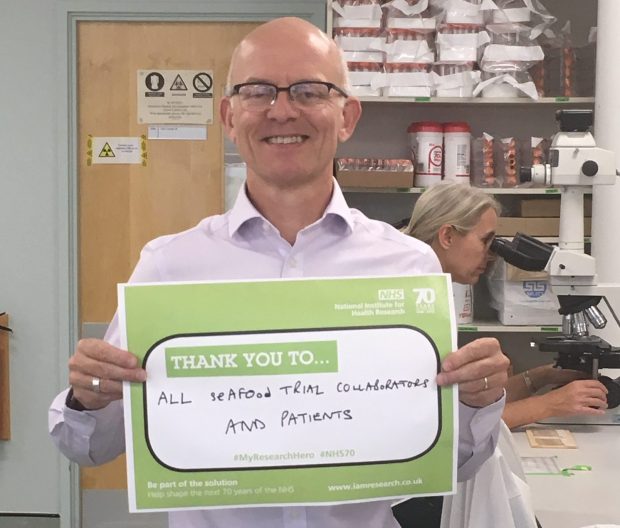 Man holding up a board which says 'thank you to all seafood trial collaborators and patients'.