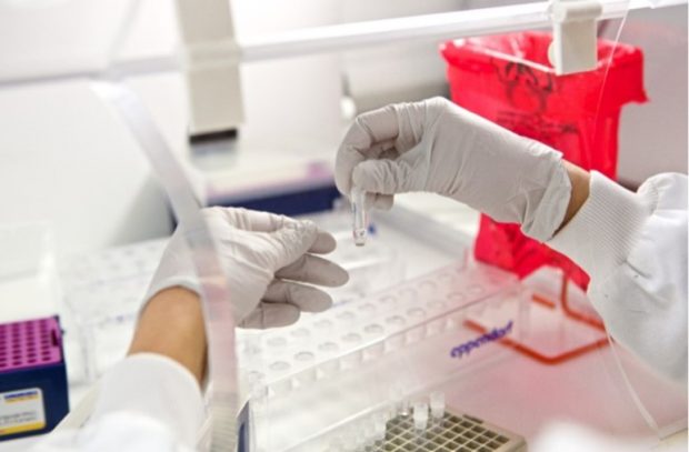 A pair of hands in a lab with plastic gloves testing samples