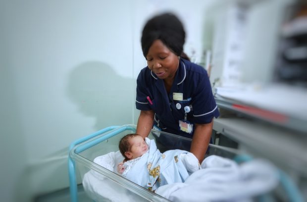 A nurse putting a newborn baby into a cot in a hospital ward