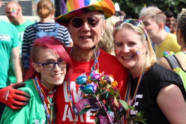 An older man with 2 younger women at a gay pride event in colourful clothes