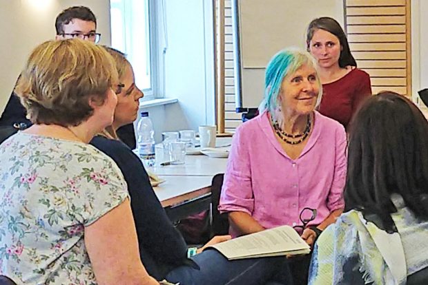 Dr Angela Raffle, wearing a pink shirt, sitting and smiling in the middle of a group of screening professionals at a screening masterclass