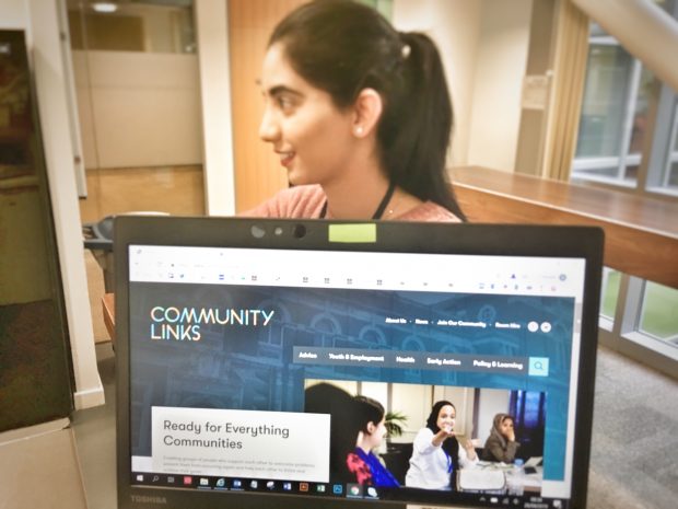 The Community Links homepage on a laptop screen and a woman in the background.