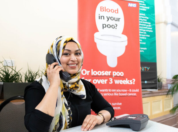 A lady on the phone smiling with information about bowel cancer in the background