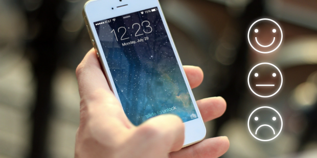 Close-up of someone holding a smartphone, with a smiley face, neutral face and unhappy face next to it.