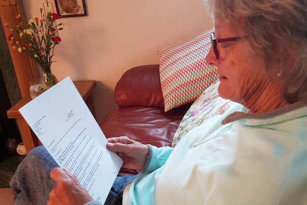 Woman is sitting in a chair reading the self-referral letter for breast screening.