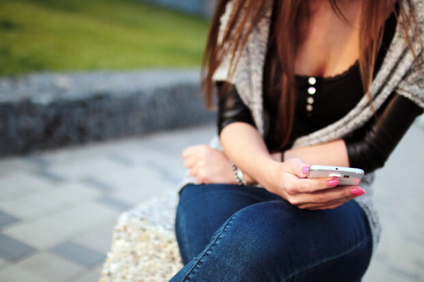 Woman holds a mobile phone in her right hand as she looks up information on it.