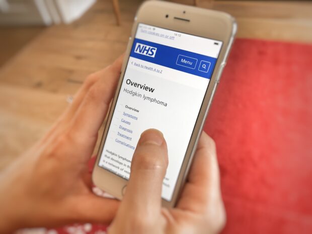 Woman's hand holding a mobile phone where she is looking up information about Hodgkin lymphoma