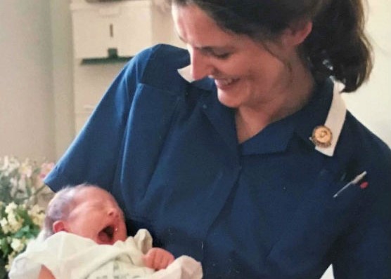  Cathy Coppinger during her years as a midwife holding a baby.