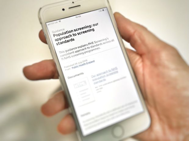 Mobile phone being held by a male hand showing population screening standards screenshot