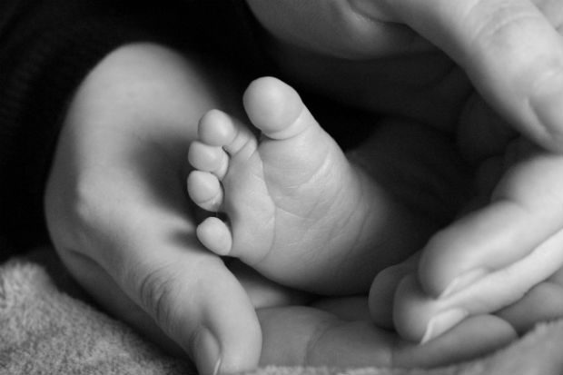 A baby's foot is seen being held by 2 adult hands.