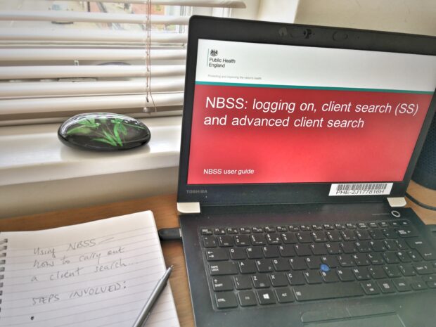 A laptop on a desk shows the words NBSS: logging on and client searches