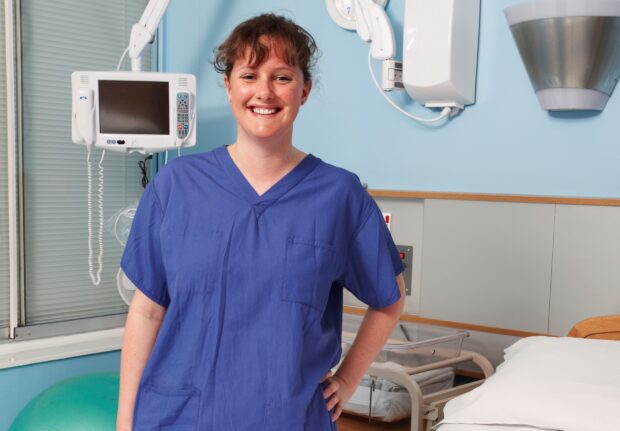 Student midwife smiling and standing by hospital bed.