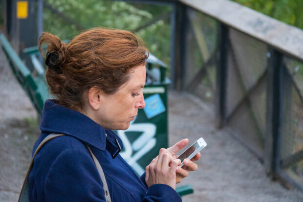 A woman sat on a bench outdoors is using her mobile phone