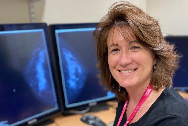 A woman smiling to camera with a breast scan on screen in the background