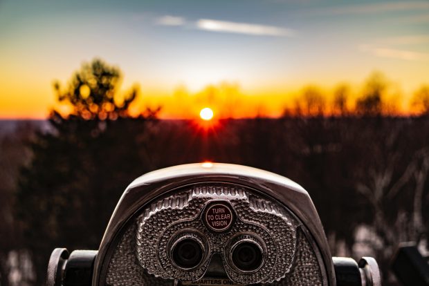 A set of public binoculars looking over a forest. The words 'turn to clear vision' are written on the binoculars.