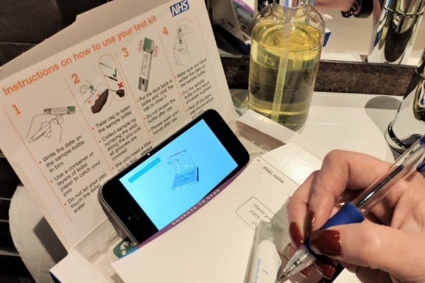 A woman writing her name on the sample tube and watching an instructional video on her mobile phone