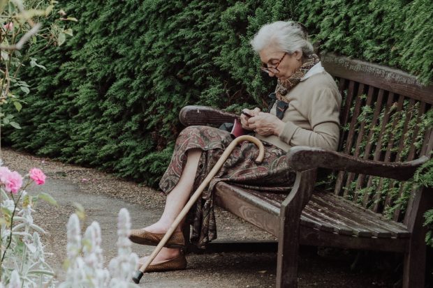 An older woman is texting while sitting on a bench