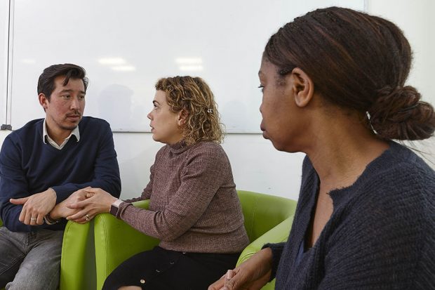 Counsellor looking at couple who are looking at each other seriously and holding hands